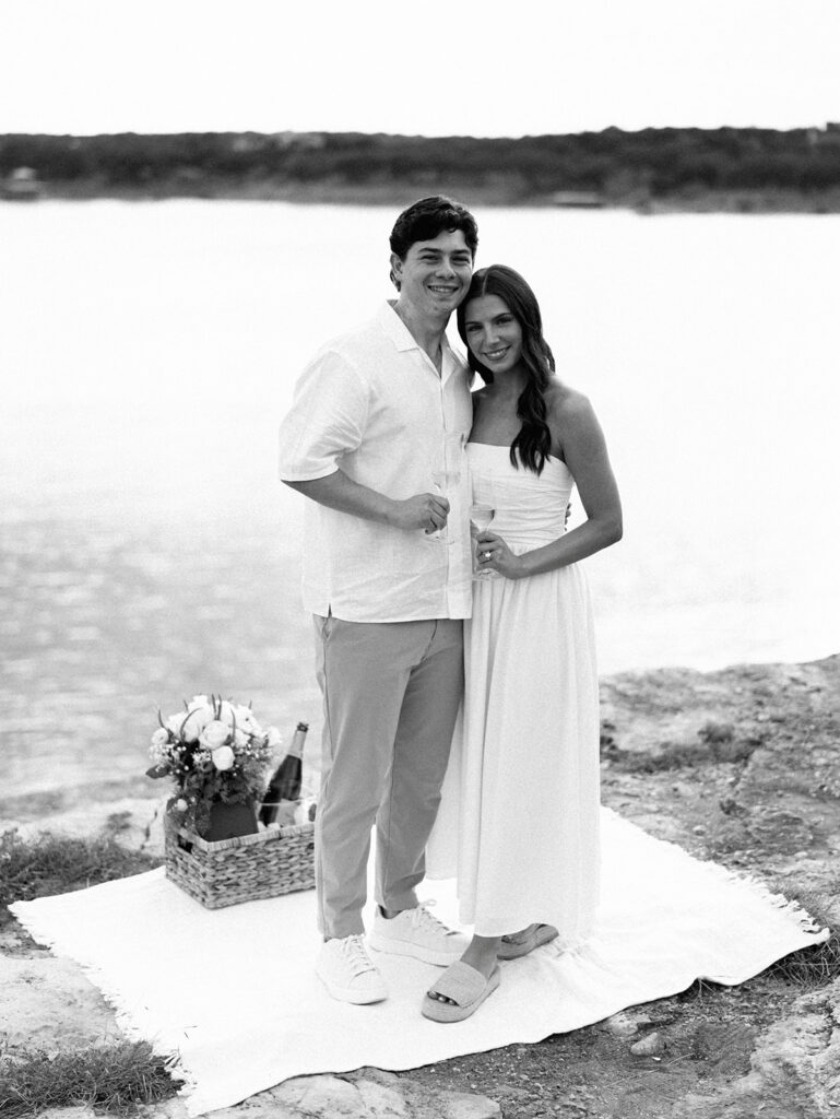Lake Travis proposal photography featuring a couple popping champagne by the lakeside after saying yes.