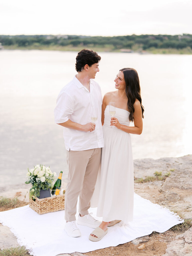 Lake Travis proposal photography featuring a couple popping champagne by the lakeside after saying yes.