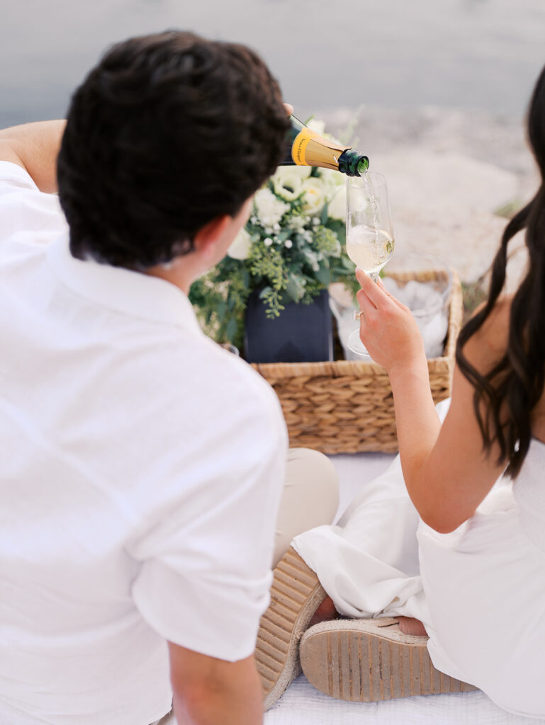Lake Travis proposal photography featuring a couple popping champagne by the lakeside after saying yes.