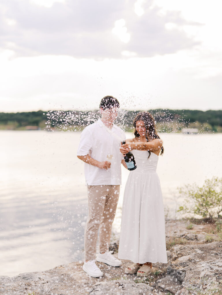 Lake Travis proposal photography featuring a couple popping champagne by the lakeside after saying yes.
