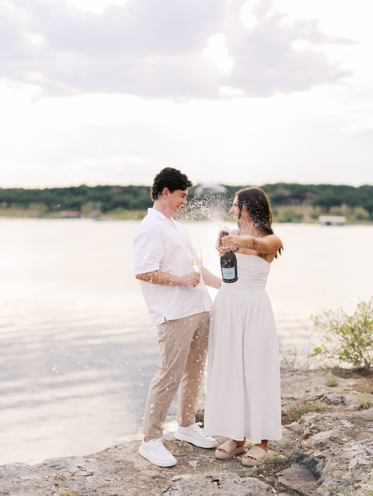 Lake Travis proposal photography featuring a couple popping champagne by the lakeside after saying yes.