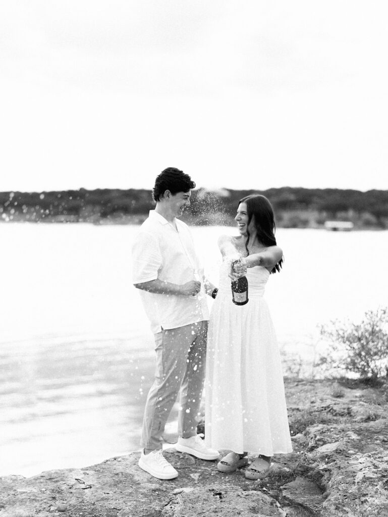 Lake Travis proposal photography featuring a couple popping champagne by the lakeside after saying yes.