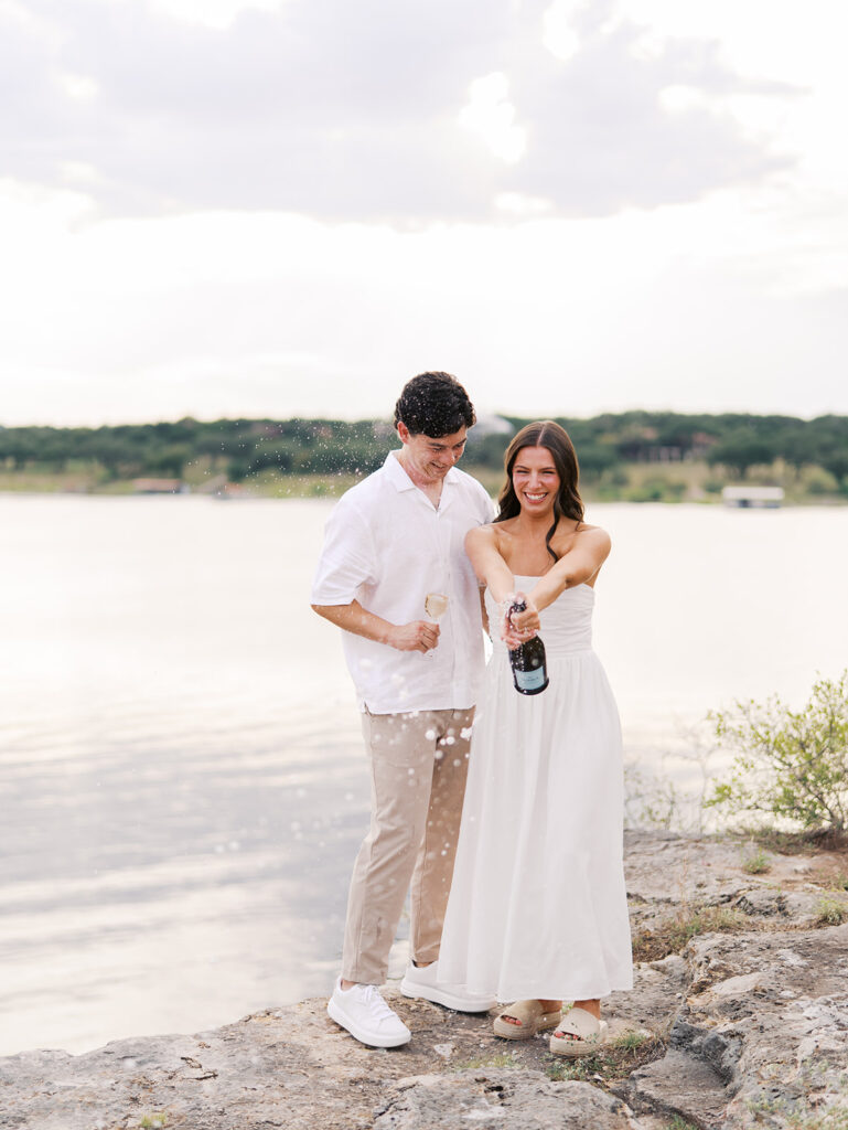 Lake Travis proposal photography featuring a couple popping champagne by the lakeside after saying yes.