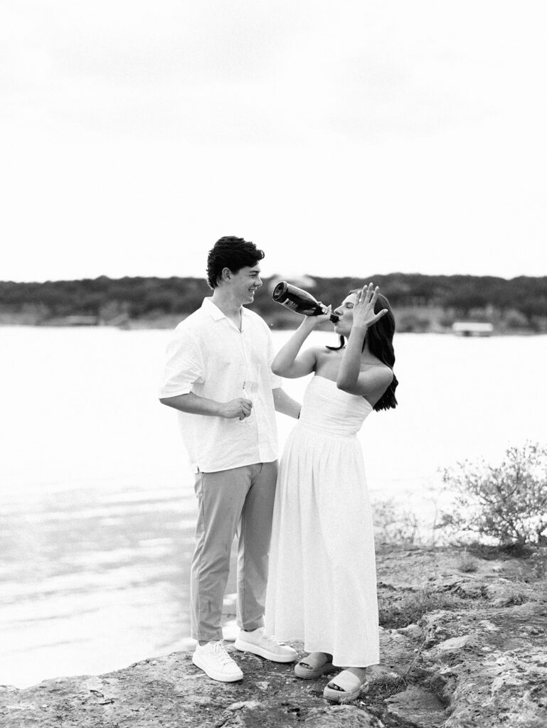 Lake Travis proposal photography featuring a couple popping champagne by the lakeside after saying yes.