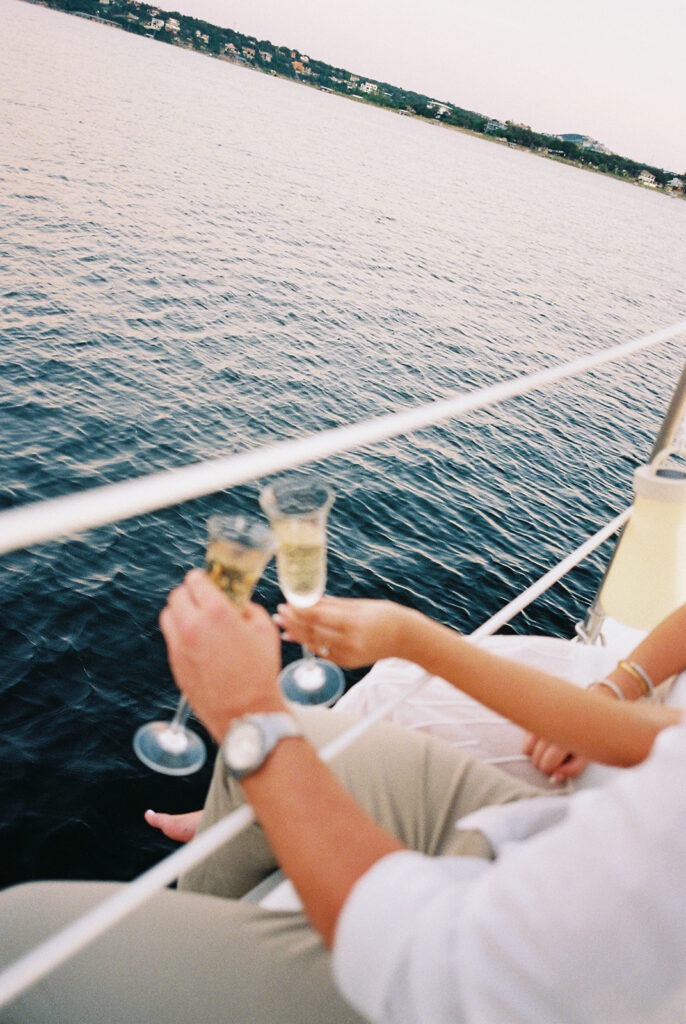 Couple popping champagne during their Lake Travis sailboat engagement session, captured at sunset.