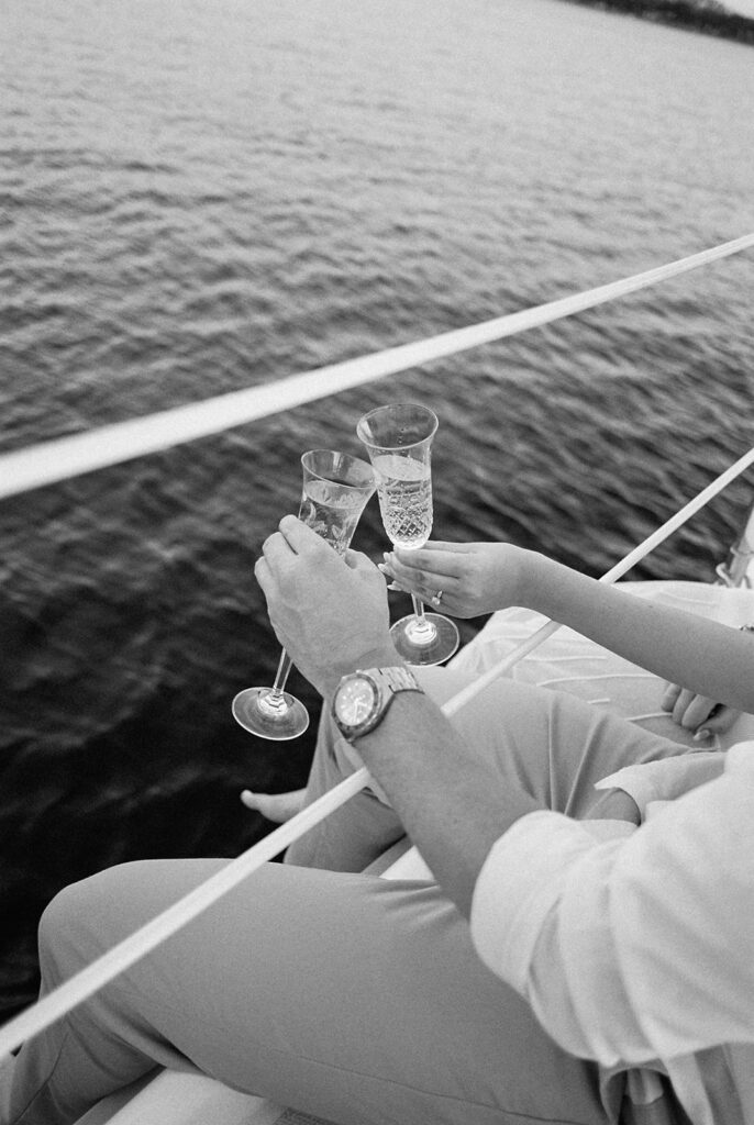 Couple popping champagne during their Lake Travis sailboat engagement session, captured at sunset.
