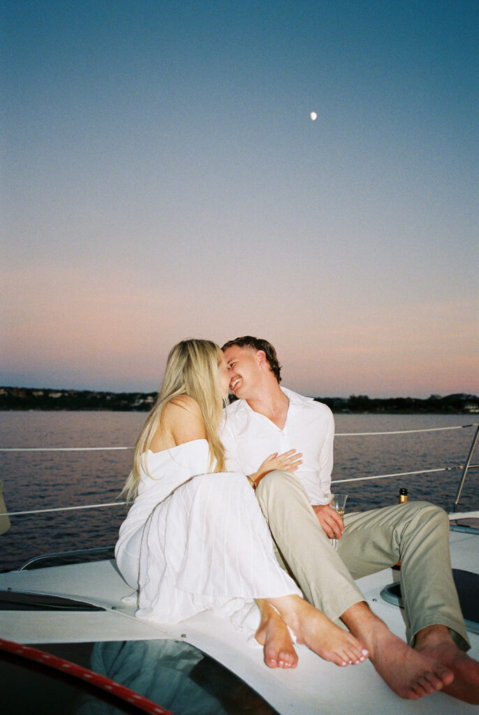 Couple popping champagne during their Lake Travis sailboat engagement session, captured at sunset.