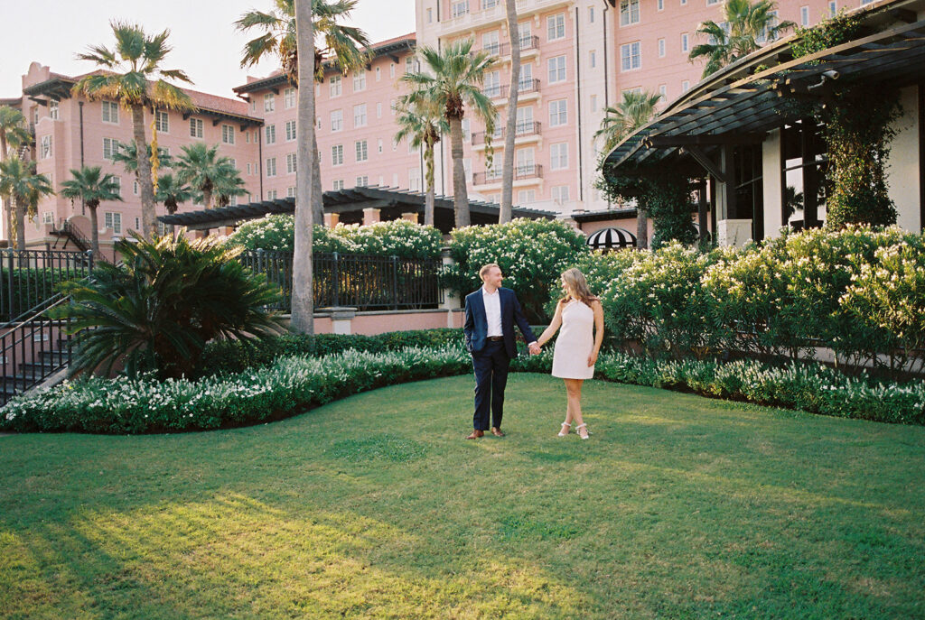 Emma and Luke smiling together in the Grand Galvez garden under tall palm trees captured on film with soft, natural light and timeless color.