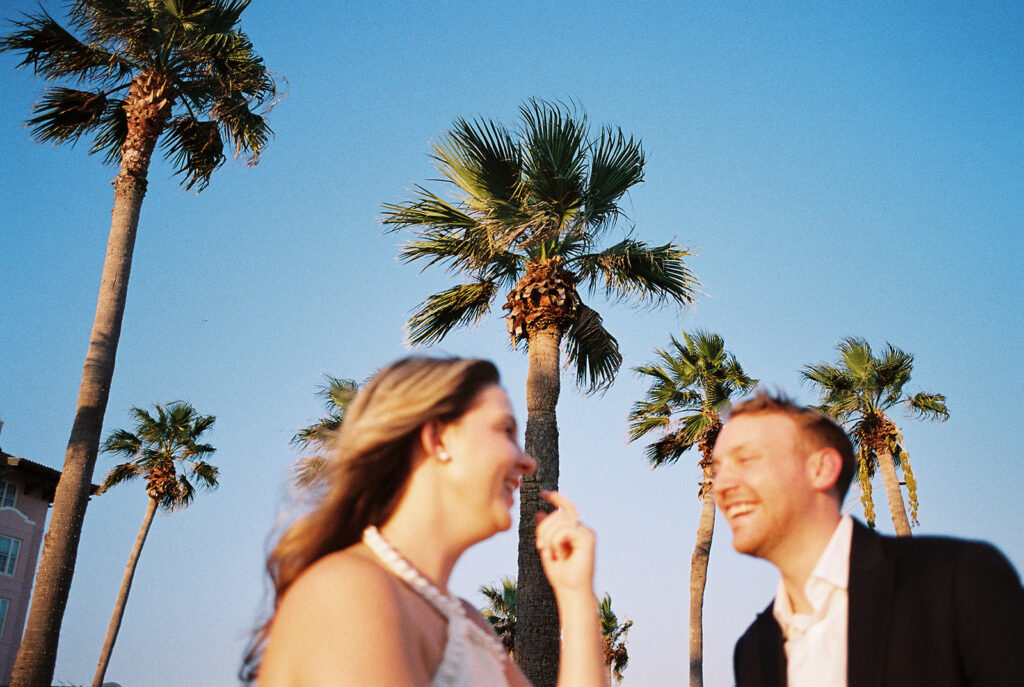 Emma and Luke smiling together in the Grand Galvez garden under tall palm trees captured on film with soft, natural light and timeless color.