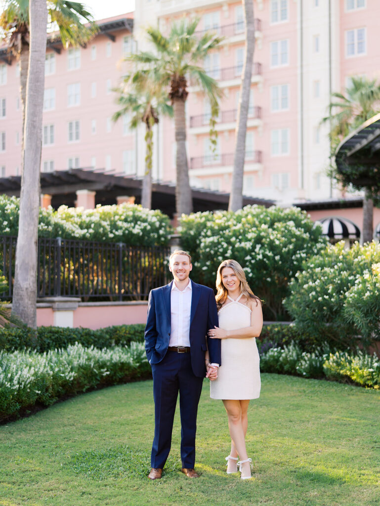 Emma and Luke smiling together in the Grand Galvez garden under tall palm trees captured on film with soft, natural light and timeless color.
