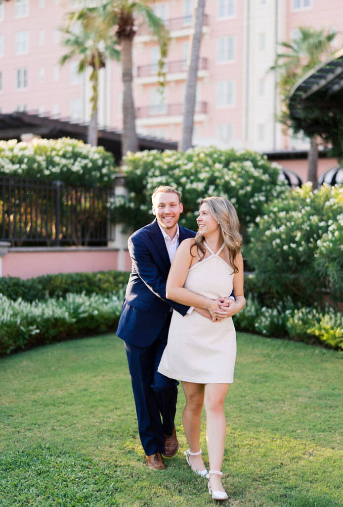 Emma and Luke smiling together in the Grand Galvez garden under tall palm trees captured on film with soft, natural light and timeless color.