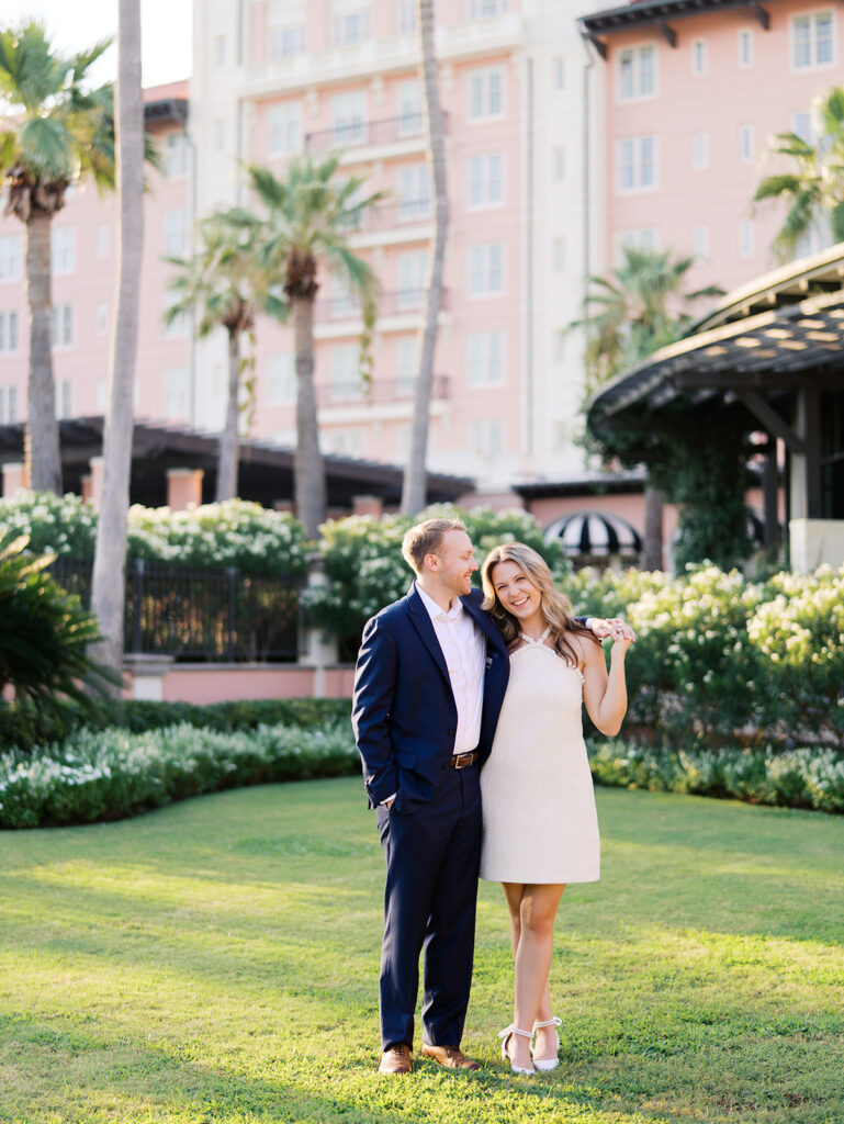 Emma and Luke smiling together in the Grand Galvez garden under tall palm trees captured on film with soft, natural light and timeless color.