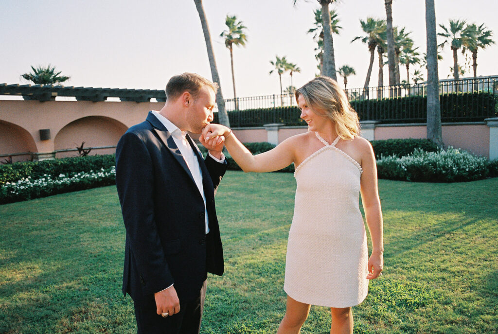 Emma and Luke smiling together in the Grand Galvez garden under tall palm trees captured on film with soft, natural light and timeless color.