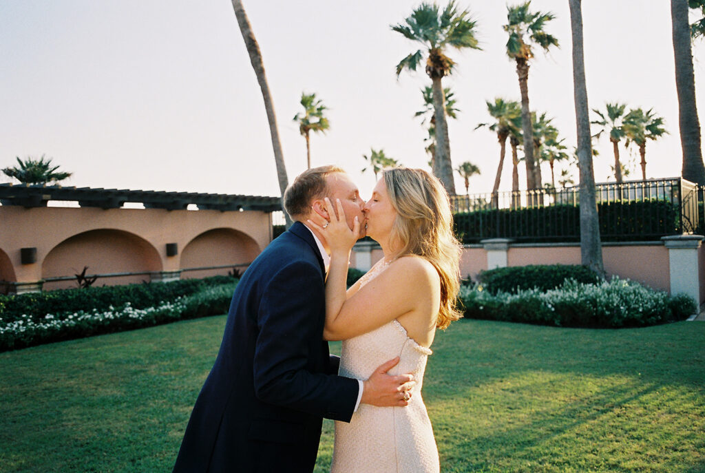 Emma and Luke smiling together in the Grand Galvez garden under tall palm trees captured on film with soft, natural light and timeless color.