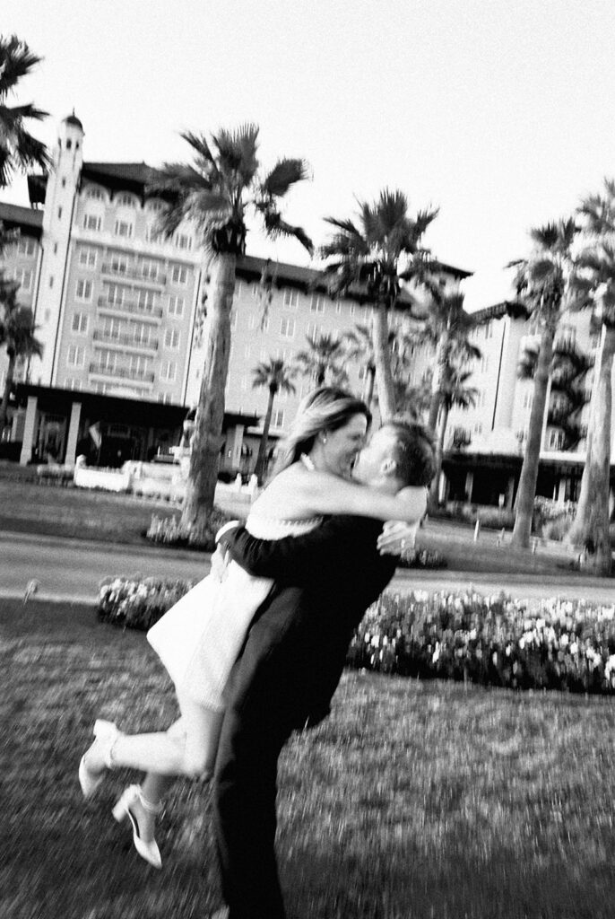 Emma and Luke smiling together in the Grand Galvez garden under tall palm trees captured on film with soft, natural light and timeless color.