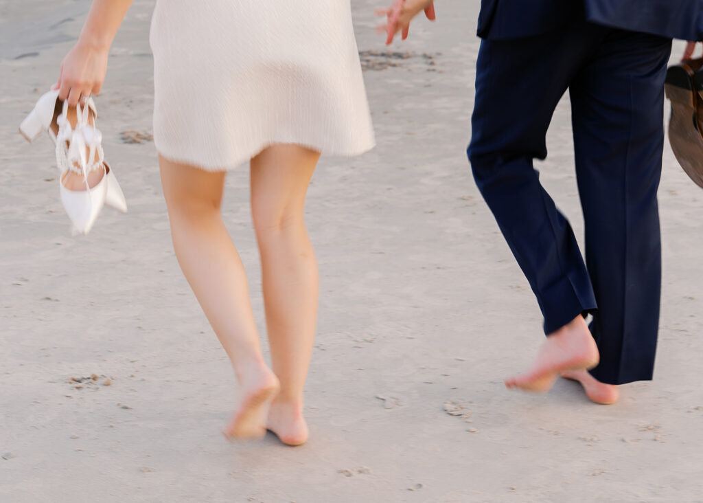 Emma and Luke walking hand in hand along the beach in front of the Grand Galvez at sunset with soft pastel tones on film
