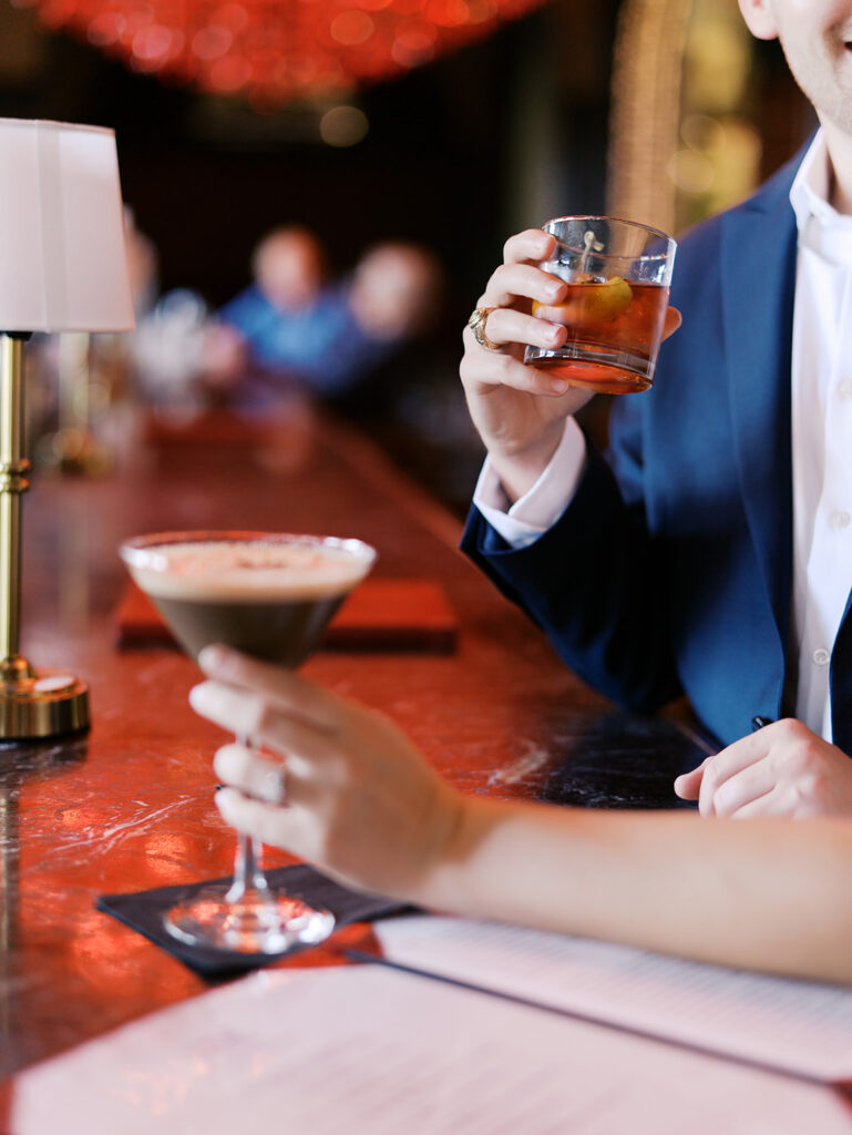 Emma and Luke cheersing and enjoying cocktails at the Grand Galvez bar photographed on film with a relaxed, romantic vibe
