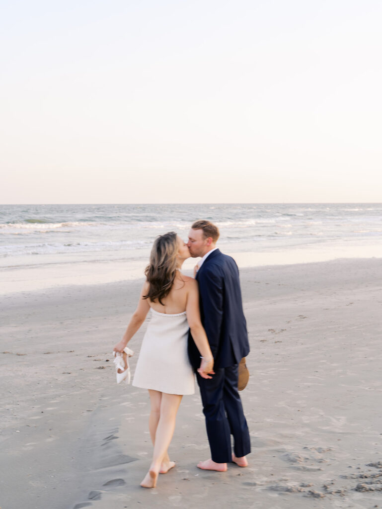 Emma and Luke walking hand in hand along the beach in front of the Grand Galvez at sunset with soft pastel tones on film
