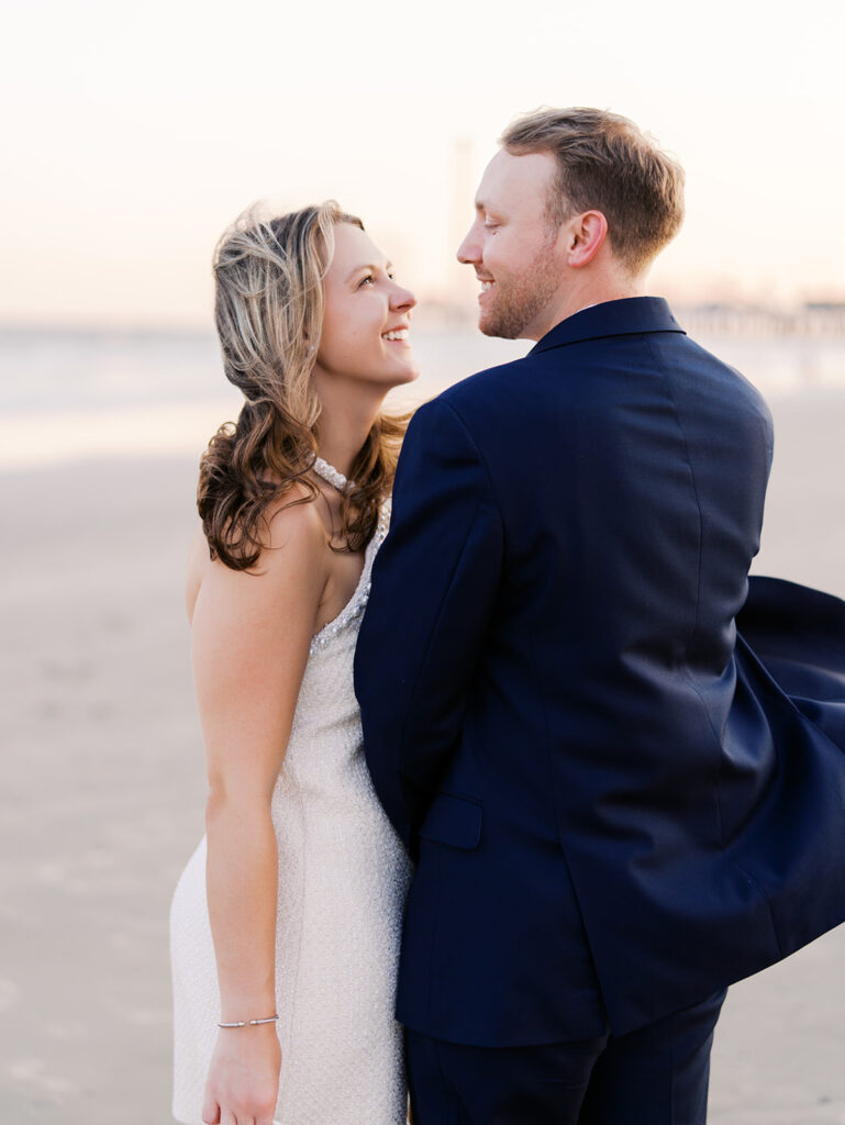 Emma and Luke walking hand in hand along the beach in front of the Grand Galvez at sunset with soft pastel tones on film