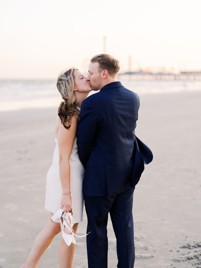 Emma and Luke walking hand in hand along the beach in front of the Grand Galvez at sunset with soft pastel tones on film