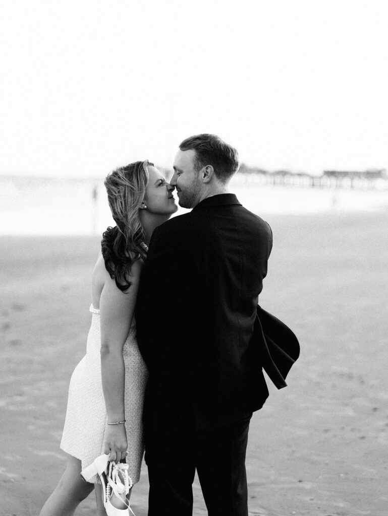 Emma and Luke walking hand in hand along the beach in front of the Grand Galvez at sunset with soft pastel tones on film