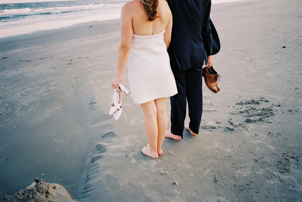 Emma and Luke walking hand in hand along the beach in front of the Grand Galvez at sunset with soft pastel tones on film