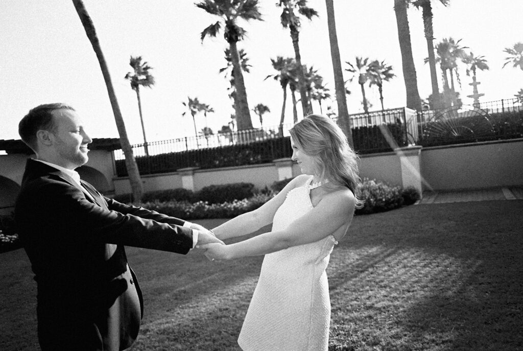 Emma and Luke smiling together in the Grand Galvez garden under tall palm trees captured on film with soft, natural light and timeless color.