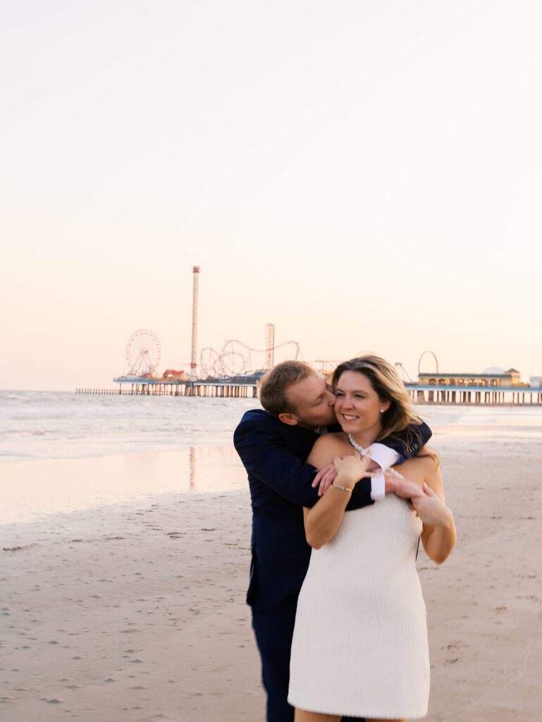Emma and Luke walking hand in hand along the beach in front of the Grand Galvez at sunset with soft pastel tones on film