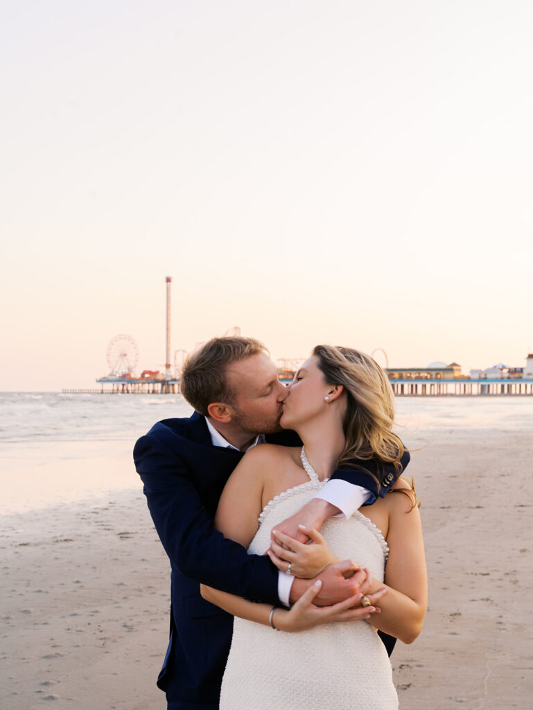 Emma and Luke walking hand in hand along the beach in front of the Grand Galvez at sunset with soft pastel tones on film