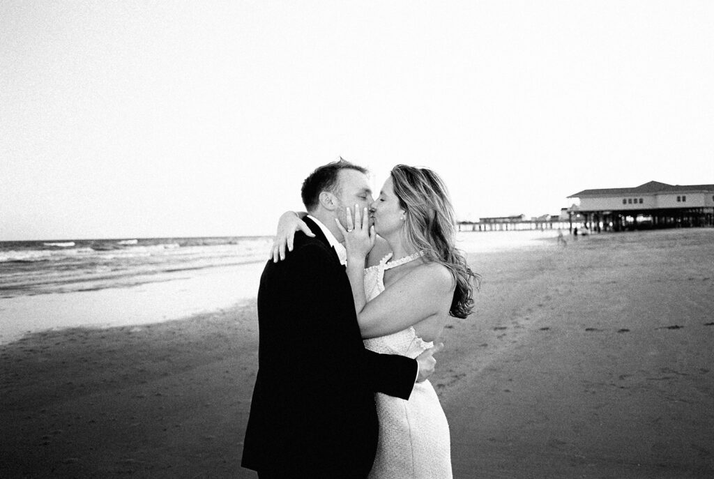 Emma and Luke walking hand in hand along the beach in front of the Grand Galvez at sunset with soft pastel tones on film