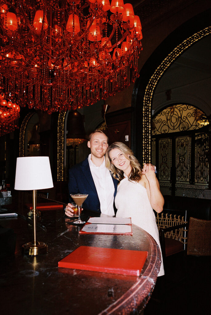 Emma and Luke cheersing and enjoying cocktails at the Grand Galvez bar photographed on film with a relaxed, romantic vibe