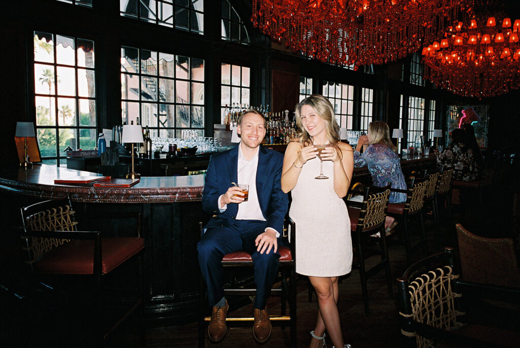 Emma and Luke cheersing and enjoying cocktails at the Grand Galvez bar photographed on film with a relaxed, romantic vibe