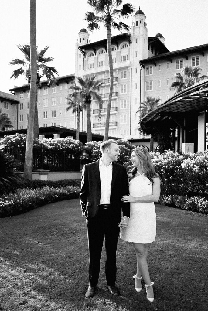 Emma and Luke smiling together in the Grand Galvez garden under tall palm trees captured on film with soft, natural light and timeless color.