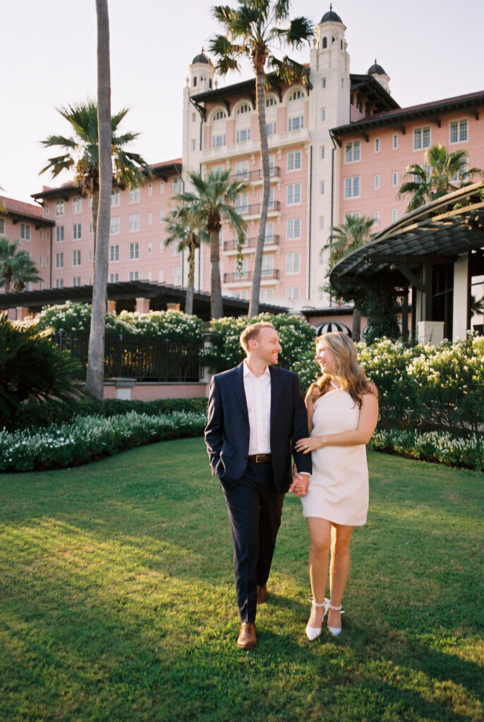 Emma and Luke smiling together in the Grand Galvez garden under tall palm trees captured on film with soft, natural light and timeless color.