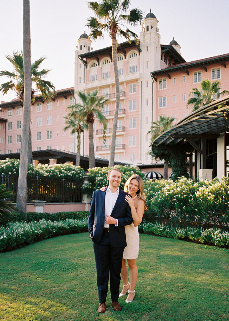 Emma and Luke smiling together in the Grand Galvez garden under tall palm trees captured on film with soft, natural light and timeless color.