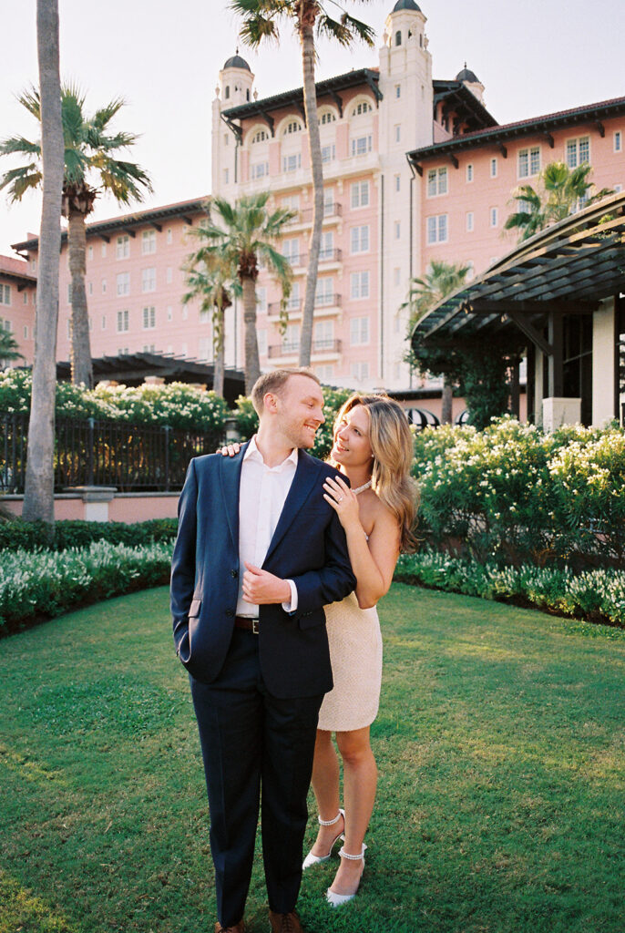 Emma and Luke smiling together in the Grand Galvez garden under tall palm trees captured on film with soft, natural light and timeless color.