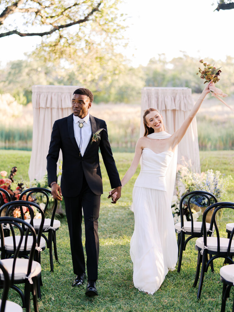 Bride and groom walking through The Addison Grove surrounded by golden fall foliage and lush florals